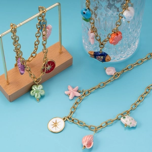 Golden chain jewelry set with starfish, fish, and flower charms on light blue background