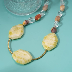 Ethnic beaded necklace with yellow green stones and metallic bars on green surface