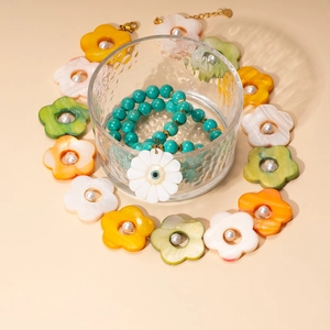 Beaded necklace with shell flower and evil eye pendant on textured glass background