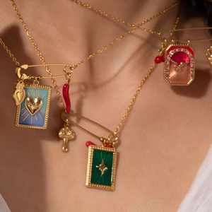 Close-up of layered gold chain necklace with colorful enamel charms and heart pendants