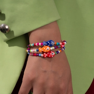 Close-up of colorful beaded bracelets with vibrant fish charms on a green blazer background
