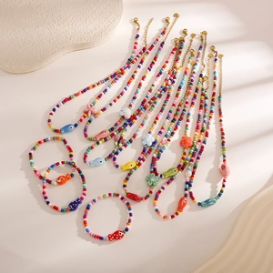 Colorful beaded necklace and bracelet set with sea life charms on a neutral stone background