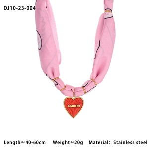 Detailed macro of the red heart pendant with gold AMOUR engraving on pink silk scarf cord
