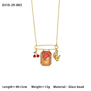 Detail of gold paperclip chain necklace with cherry, bird plaque, and hand charms