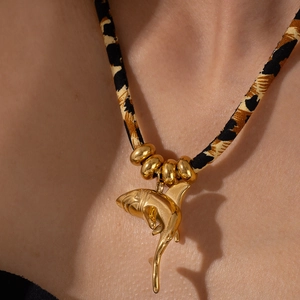 Macro view of a gold shark pendant on a leopard print rope necklace with golden beads