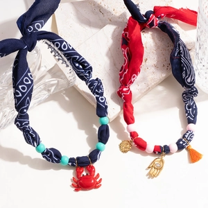 Bohemian silk scarf necklaces with crab and palm charms on a stone and glass background