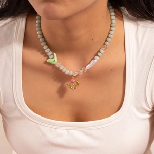 Detail of beaded necklace with green beads, baroque pearl, and gold bird charm pendant