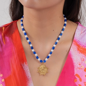 Détail du pendentif oiseau doré sur un collier de perles bleues et blanches sur modèle