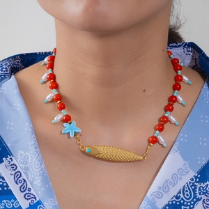 Gros plan du collier style océan avec pendentif poisson doré, perles rouges et blanches