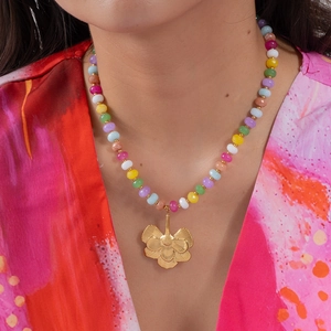 Détail d'un collier de perles colorées avec pendentif fleur dorée porté par un mannequin