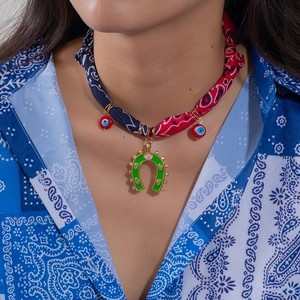Detail of a silk bandana necklace with a green horseshoe charm and evil eye beads