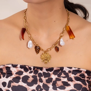 Detail of chunky gold chain necklace with leopard heart and tiger eye stone charms on a model