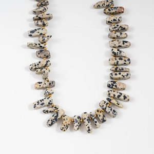 Close-up of Dalmatian Jasper stone beads with gold spacer beads on a steel chain necklace