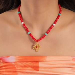 Tropical beaded necklace with red textured beads and a gold coconut tree pendant on a model