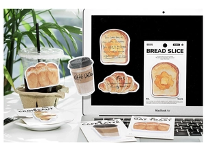 Artistic bread and coffee themed stickers arranged on a laptop keyboard and workspace