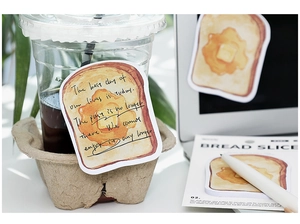 Detail of hand-drawn toast stickers applied on a coffee cup and notebook surface