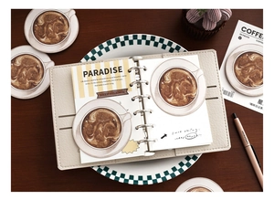 Macro detail of coffee-themed stationery stickers on a cream leather binder cover