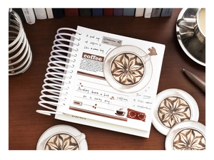 Macro detail of coffee-themed spiral notebook with latte art on a vintage wooden desk
