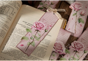Detailed shot of vintage pink rose bookmarks with lace on an antique book and wood table