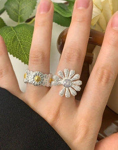 Detailed view of silver daisy rings set with sparkling zircons and yellow enamel floral accents