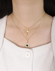 Detailaufnahme einer goldfarbenen Halskette mit Pferdeanhänger und schwarzer Münze