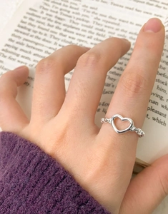 Close-up of S925 sterling silver hollow heart ring worn on a hand against book pages