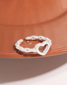 Detailed close-up of a silver chain ring with a minimalist hollow heart on ceramic plate