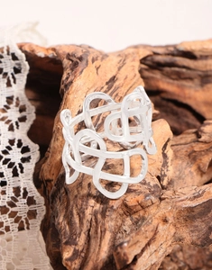 Detail of wide hollow woven ring in 925 sterling silver on a rustic wooden background