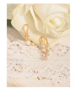 Detail shot of golden bow earrings with white pearl and zircon on white roses