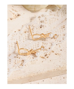 Close-up of gold-plated knot earrings with white pearls and square zircon accents
