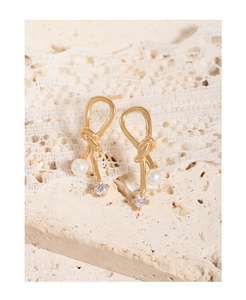 Close-up of golden bowknot stud earrings with pearl and zircon on stone background