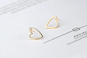 Detailed close-up of gold hollow heart stud earrings with tiny zircon accents