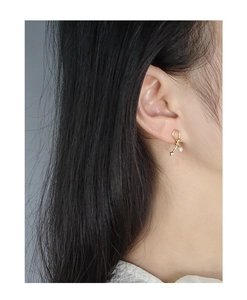 Elegant gold bow earrings with white pearl and sparkling zircon on model's ear