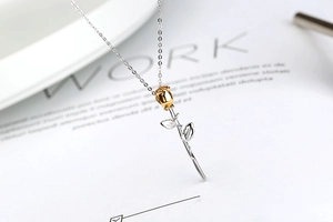 Macro detail of golden rose flower pendant with silver stem on delicate chain necklace