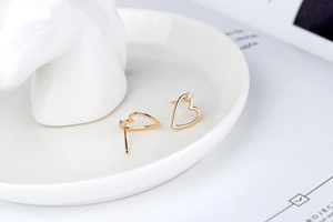 Close-up of heart-shaped gold stud earrings with cubic zirconia on white ceramic tray