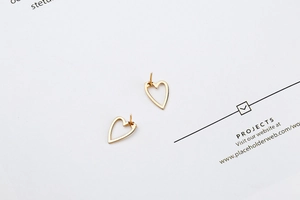 Detailed close-up of hollow heart stud earrings in polished gold finish with zircons