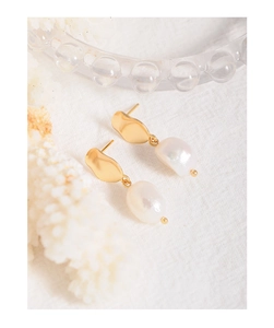 Detailed close-up of Baroque pearl earrings with textured gold plates on white fabric