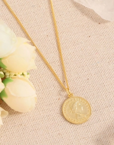 Détail d'un collier pièce dorée avec profil de reine sur un fond beige texturé élégant