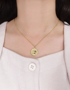 Gros plan détaillé d'un collier pendentif pièce d'or Elizabeth II sur un pull blanc