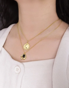 Détail de colliers dorés superposés avec pendentif pièce et pierre noire