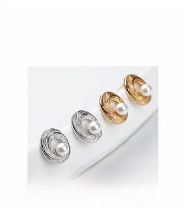 Detailed macro view of spiral textured silver and gold pearl stud earrings on a white stand