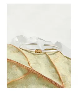 Detail of 925 sterling silver open bangle with a small golden smiling face charm