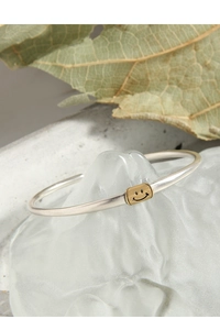 Macro detail of 925 sterling silver open bracelet with golden smiley face bead on art base