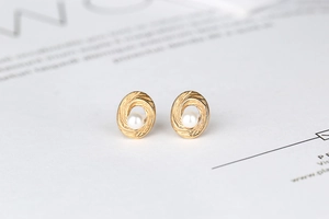 Macro view of gold spiral texture earrings with white pearl inlay on white background