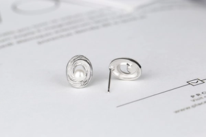 Macro view of spiral silver stud earrings with pearl centers on minimalist background