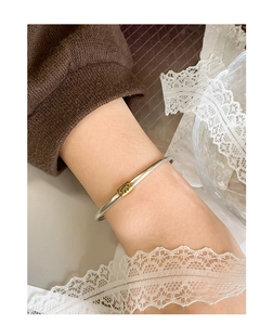 Detail of silver bangle featuring a gold rectangular charm with a black smiley face icon