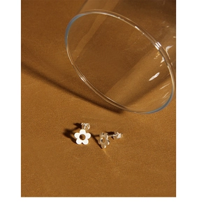 Macro detail of minimalist silver floral stud earrings with hollow petal design on sand