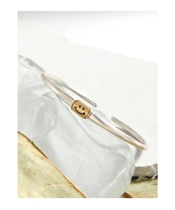 Detailed view of silver smile face open bangle on a textured white stone base