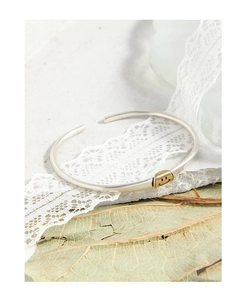 Detail of a 925 silver open cuff bracelet featuring a minimalist golden smiley face charm