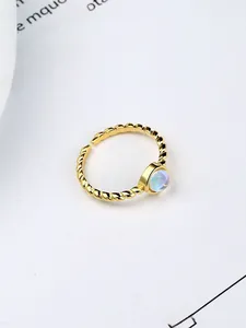 Macro detail of adjustable gold twisted rope ring featuring a round blue moonstone